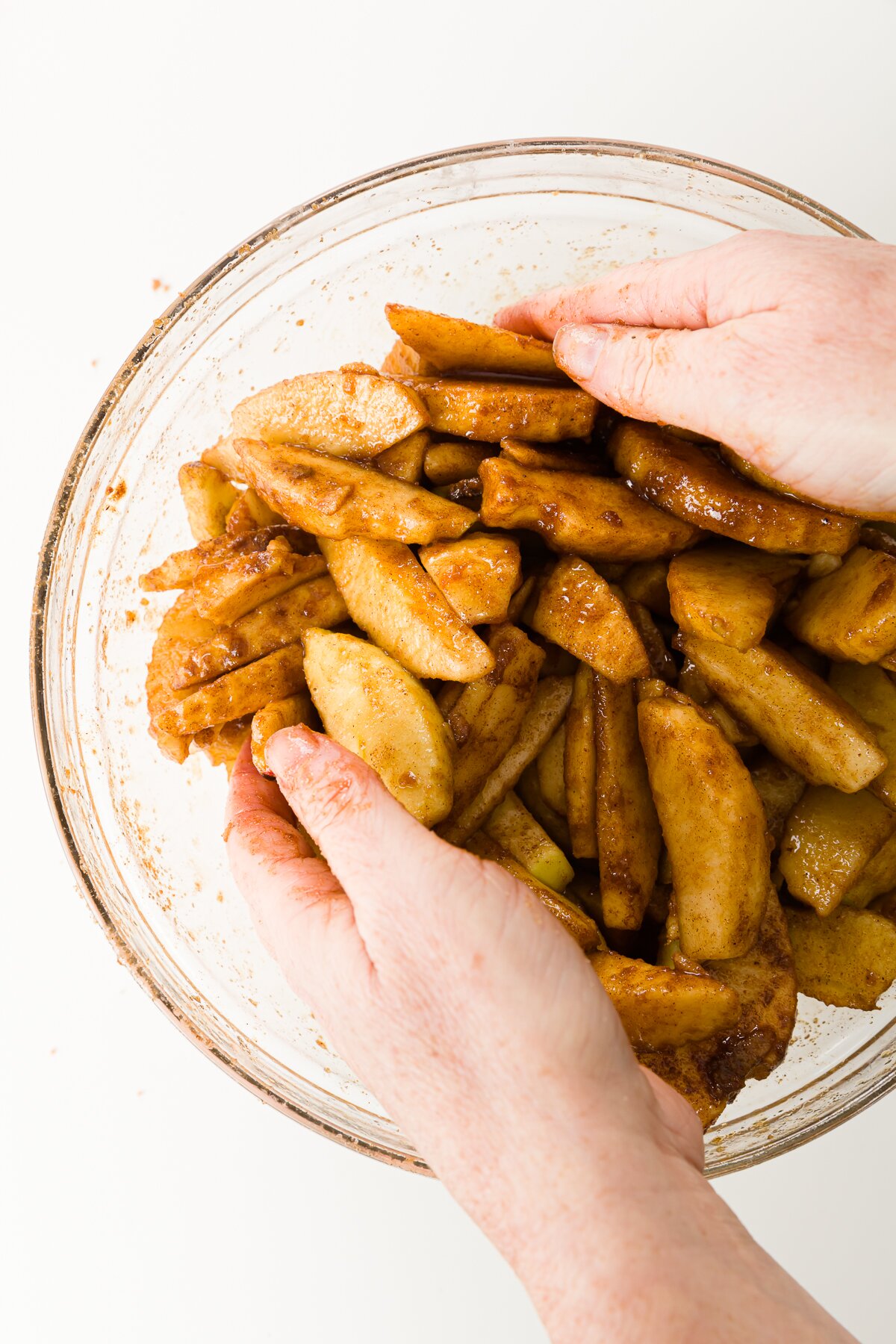 Using hands to toss apples with spices in a glass bowl