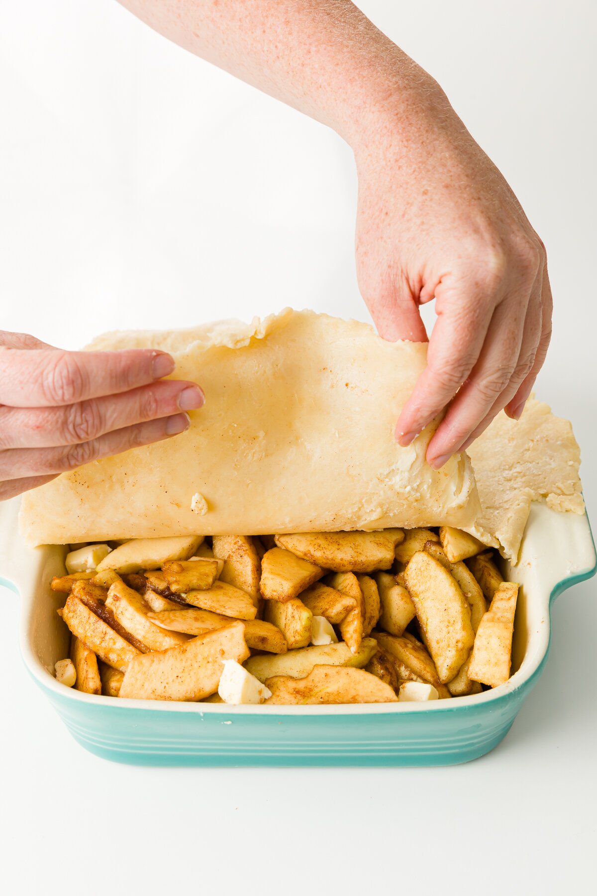 Placing pie crust over the top of apples in baking pan
