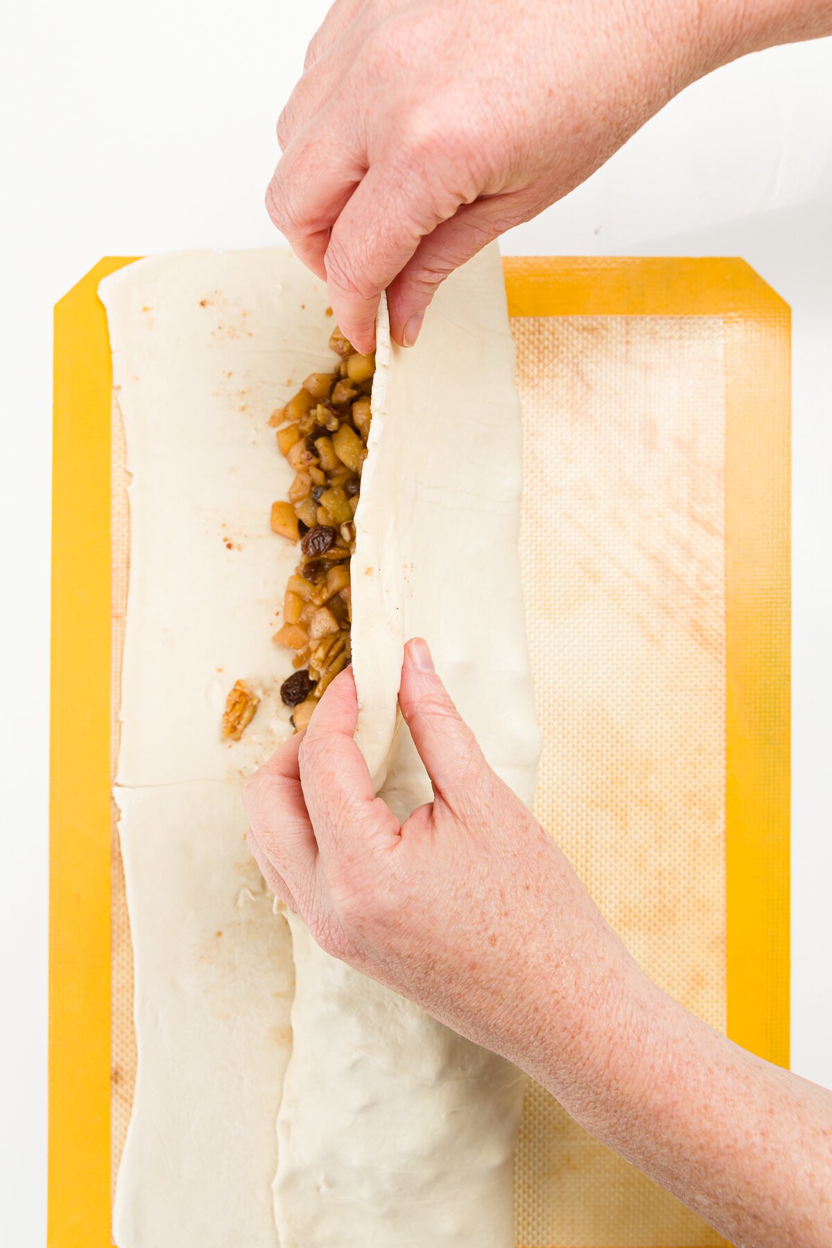 Folding puff pastry over apple filling on a yellow silicone mat