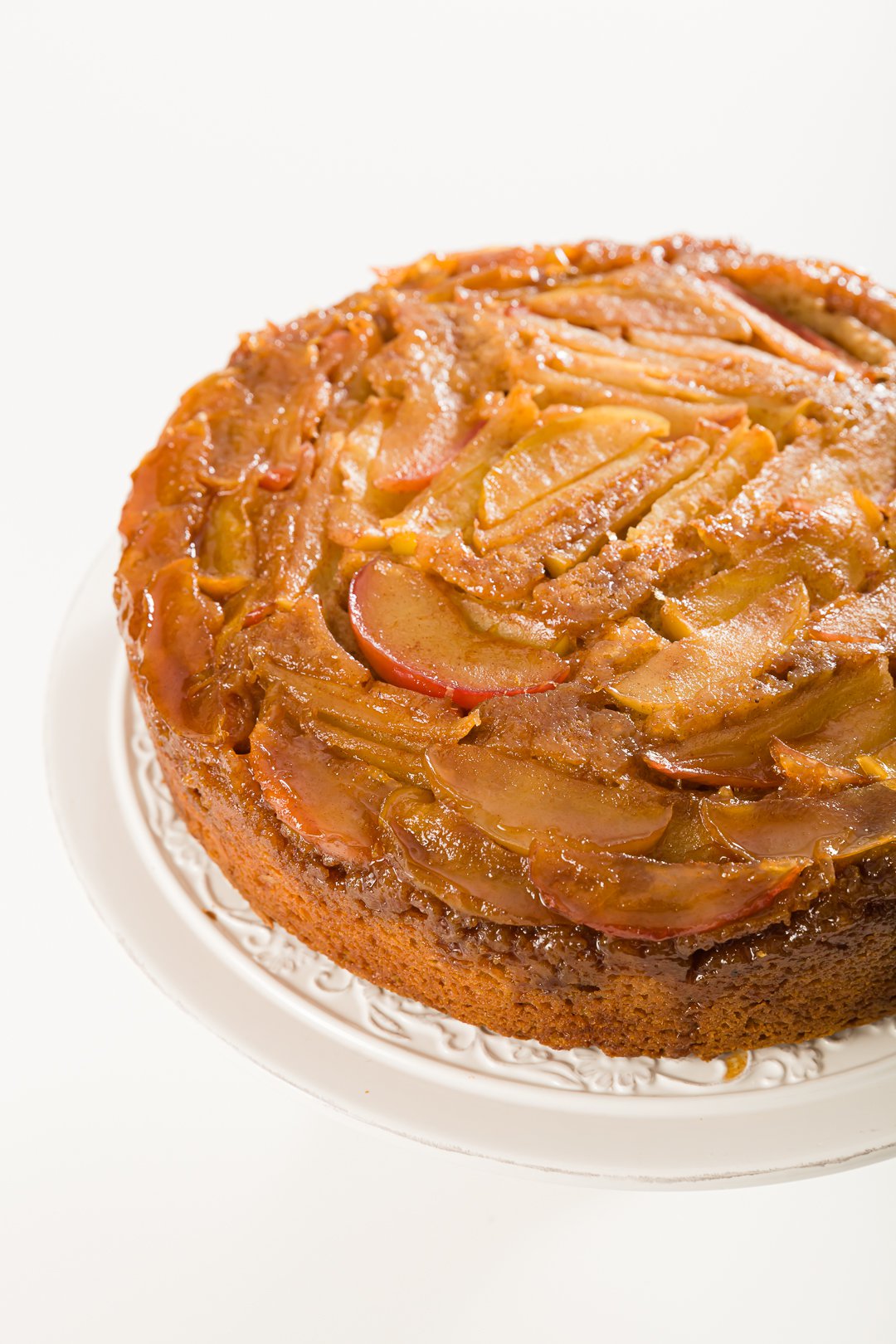 Overhead shot of apple upside-down cake unsliced on a white cake stand