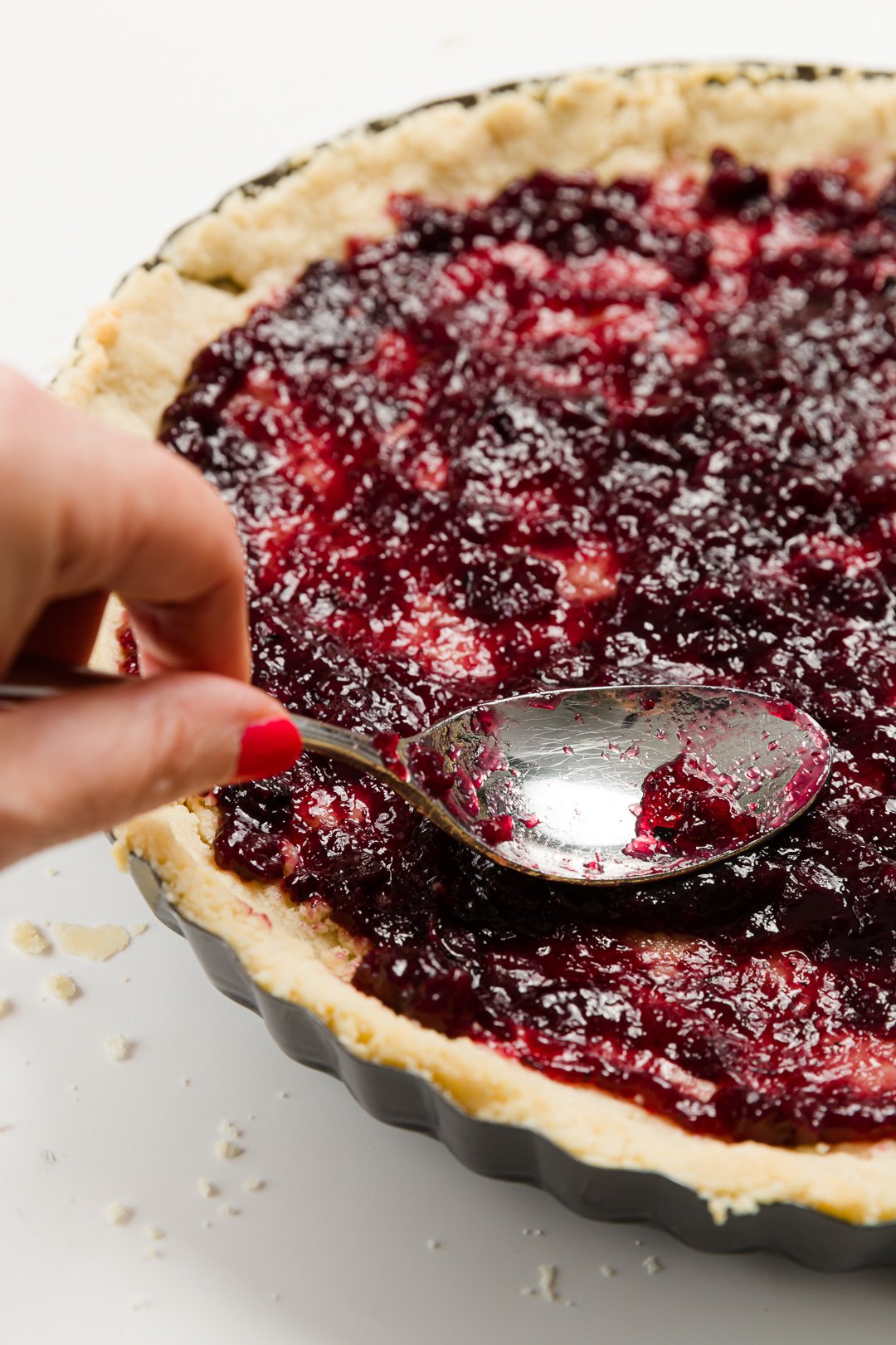 Spreading jam on an unbaked tart using the back of a spoon
