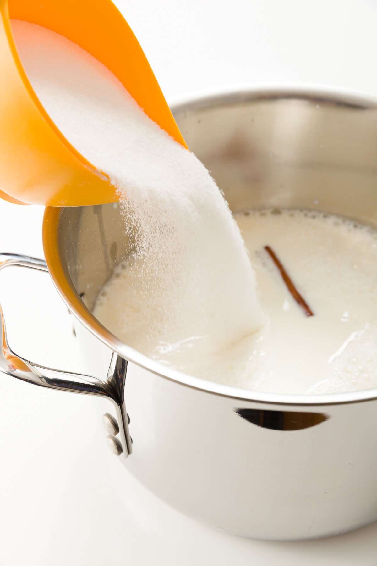 view of sugar being added to a pot with other cajeta ingredients