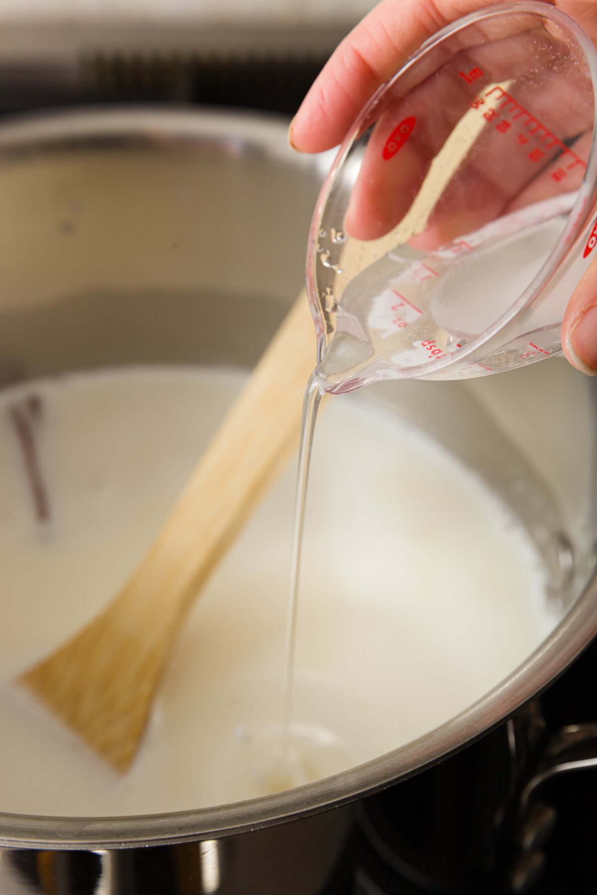 view of Stef pouring a slurry of baking soda and water into a pot full of cajeta ingredients