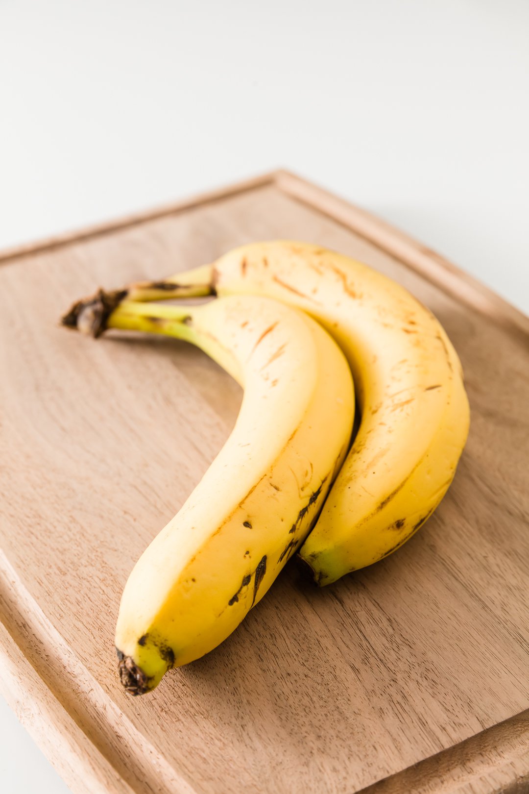 Two yellow bananas with just a few brown spots on a cutting board