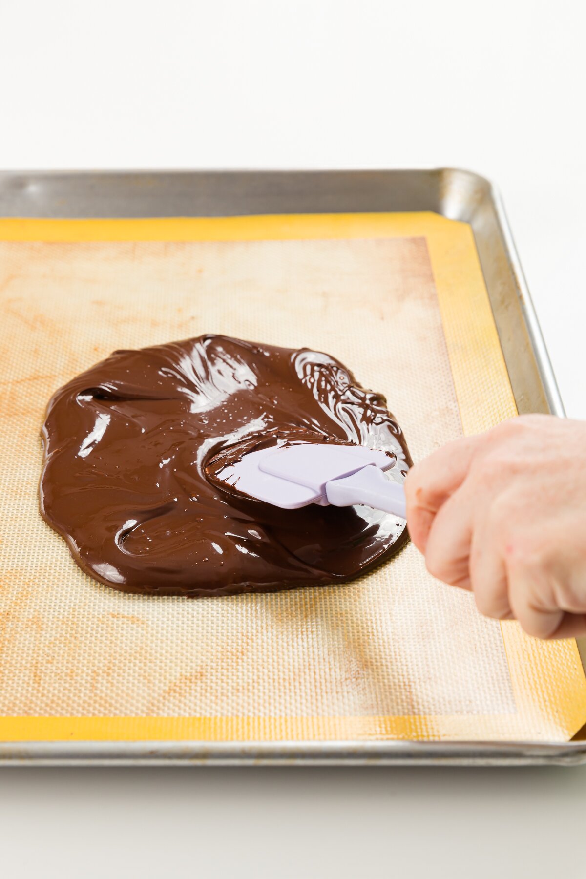 Spreading melted chocolate with a spatula on a silicone mat on a cookie sheet