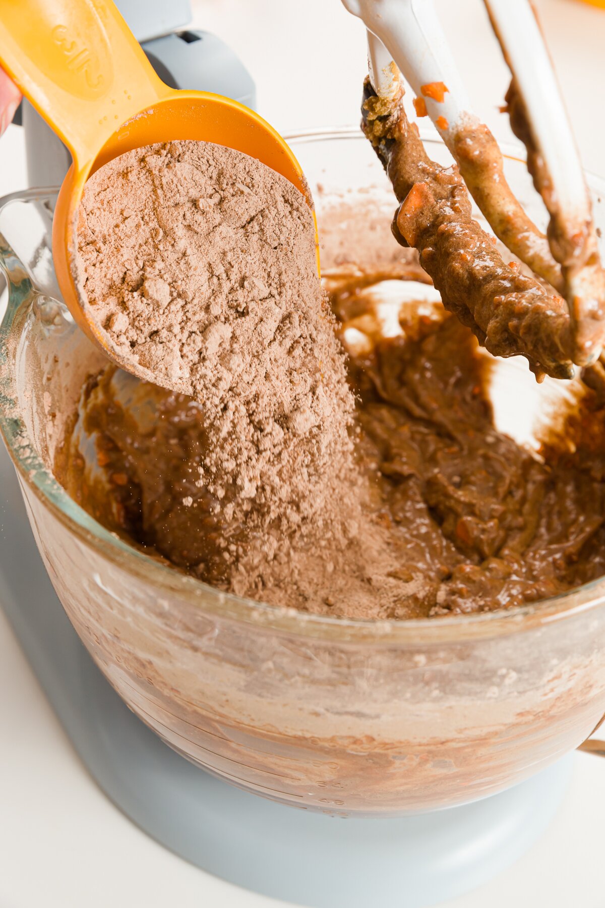 Adding dry ingredients to the bowl of a stand mixer from a yellow measuring cup