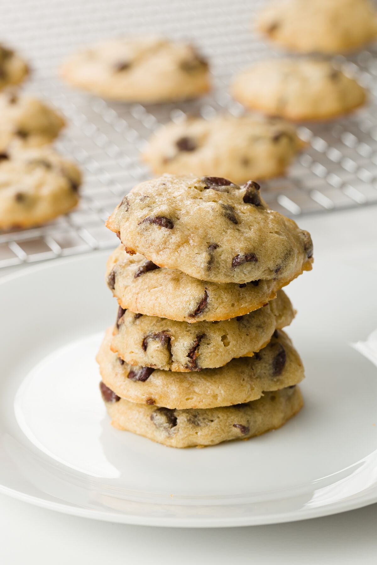 Stack of cookies on a white plate with a cooling rack of cookies in the background