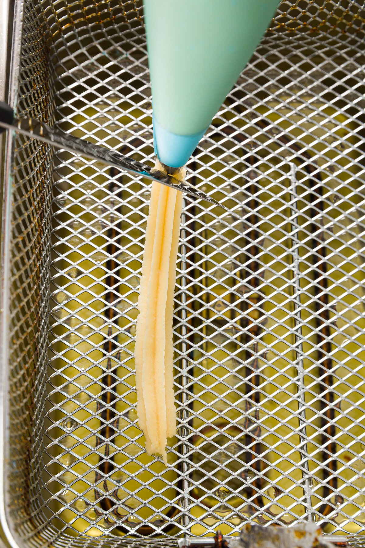 Piping churros into a fryer basket and cutting the end with a knife