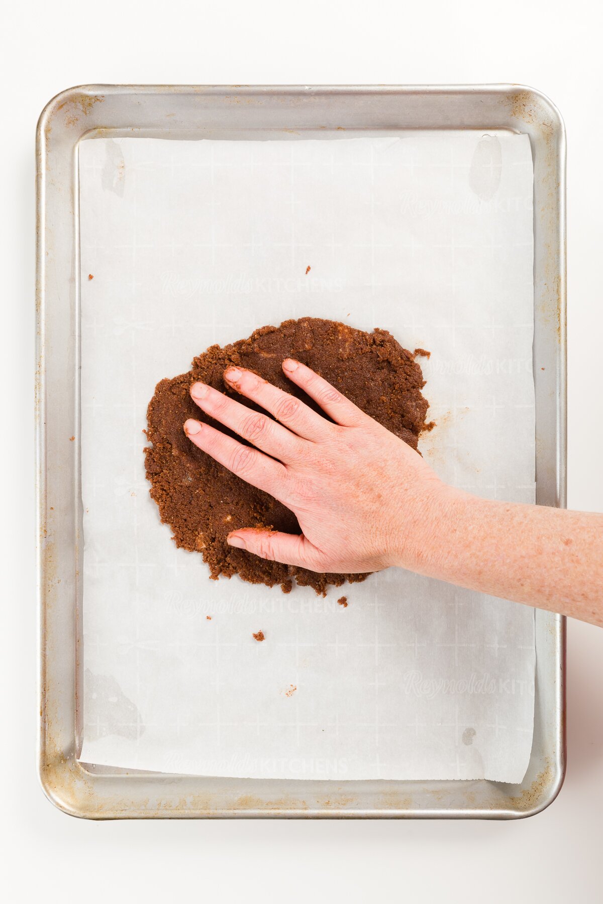 Pressing brown sandy mixture onto parchment paper on a cookie sheet
