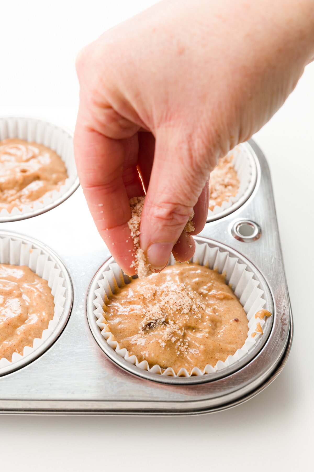 sprinkling cinnamon sugar over muffin batter in muffin tin