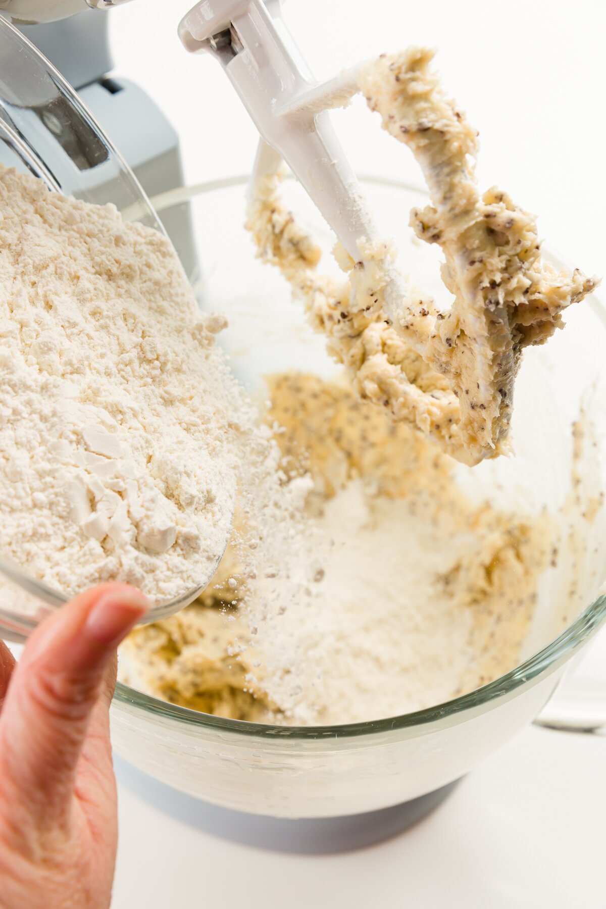Pouring flour into a mixing bowl of a stand mixer with dough on the blade