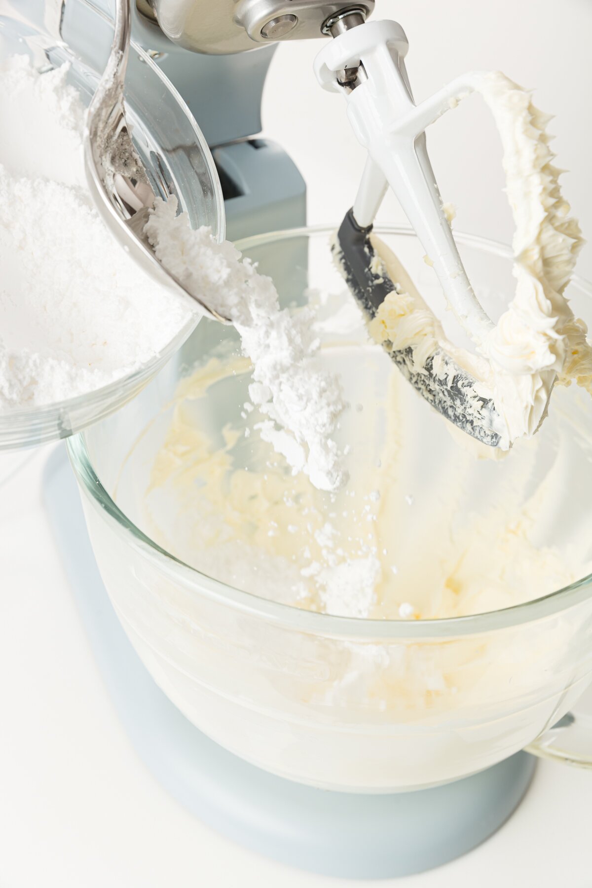 Pouring powdered sugar into a stand mixer with the beater blade raised