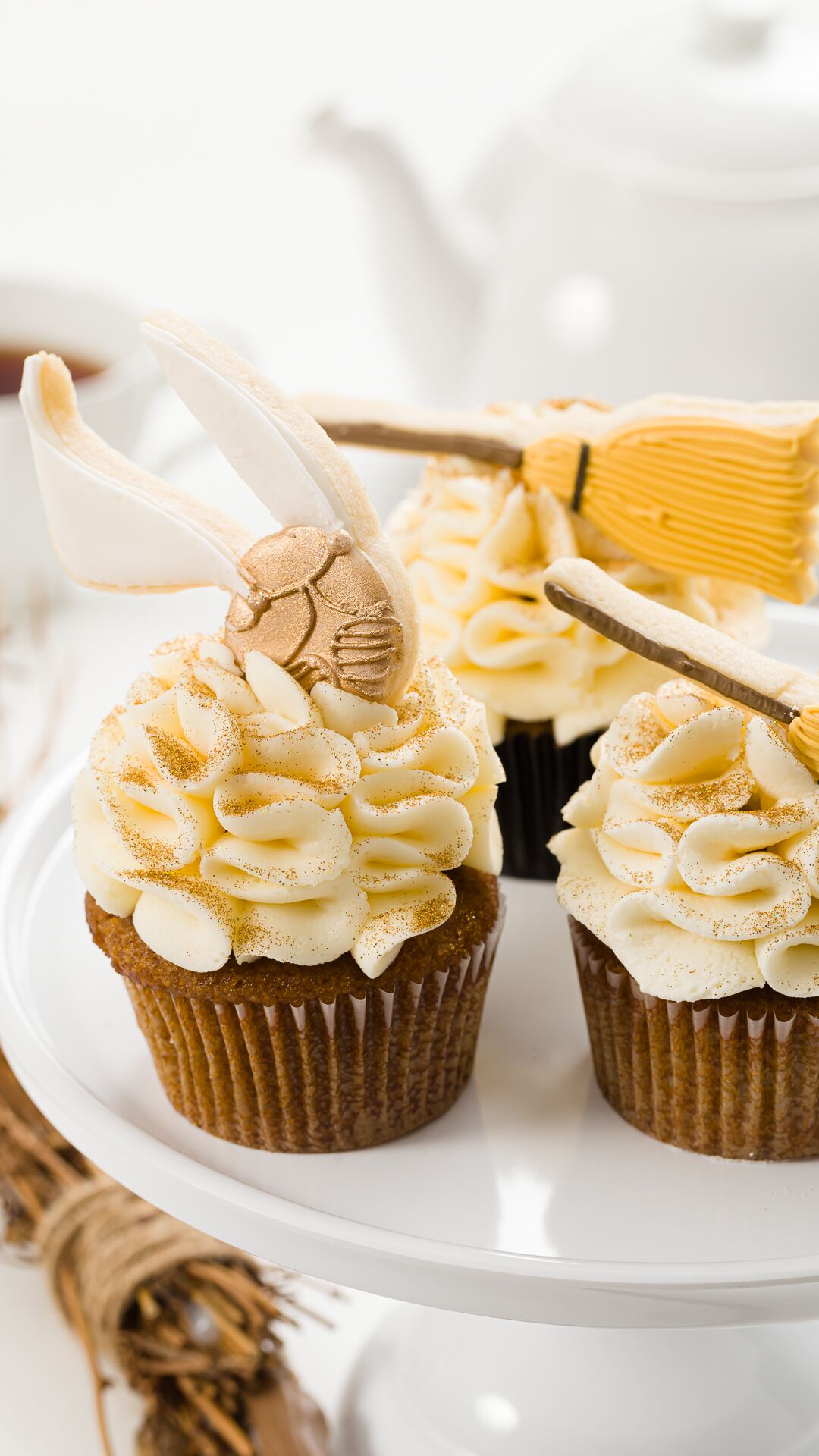 Cupcakes on a white stand with vanilla frosting topped with cookie brooms and sniches