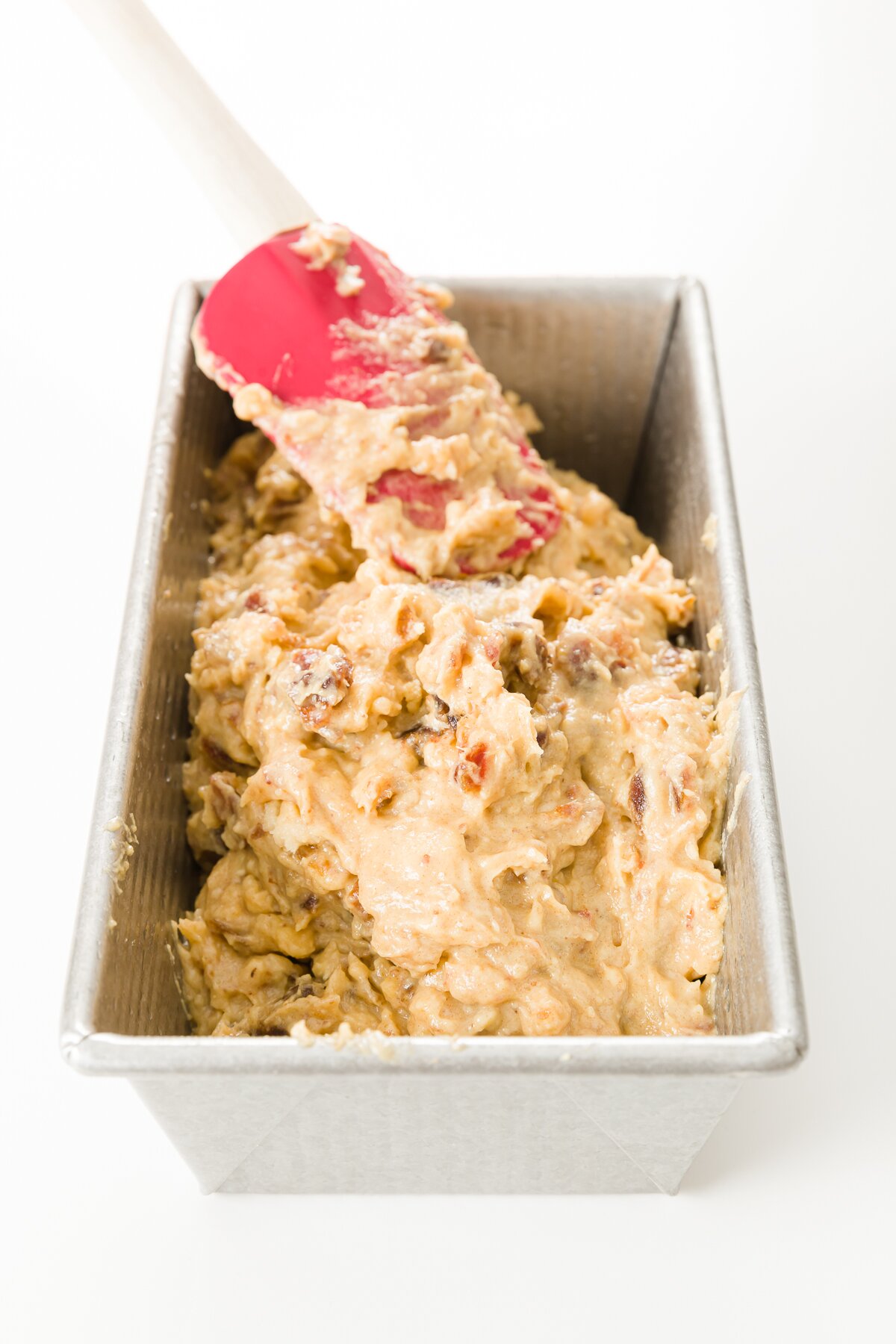 Spreading batter in a loaf pan with a red spatula