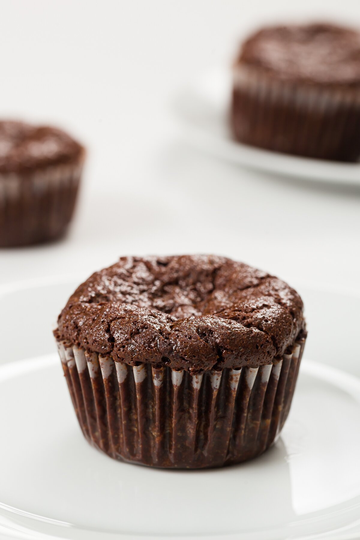 flourless chocolate cupcake on a plate with no topping and other cupcakes in the background