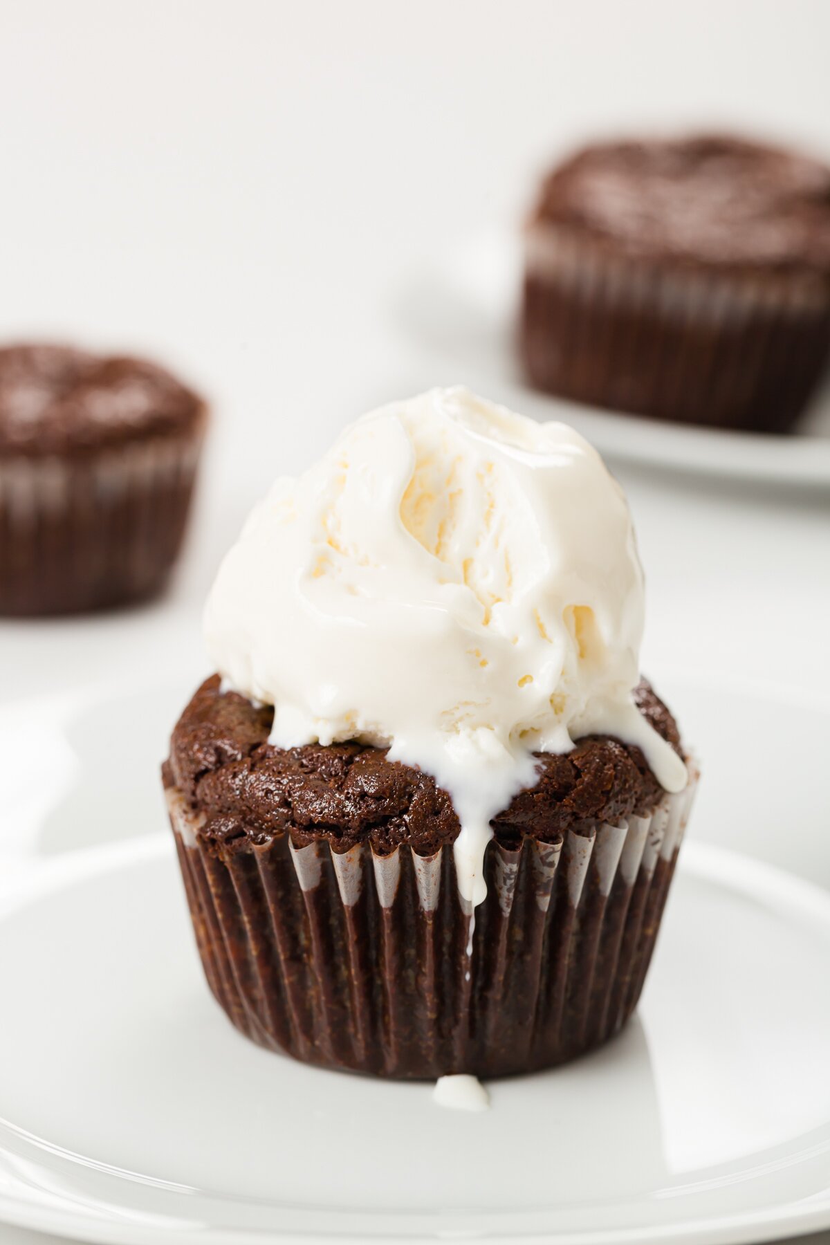 flourless chocolate cupcake with melty vanilla ice cream cream on top and some cupcakes in the background