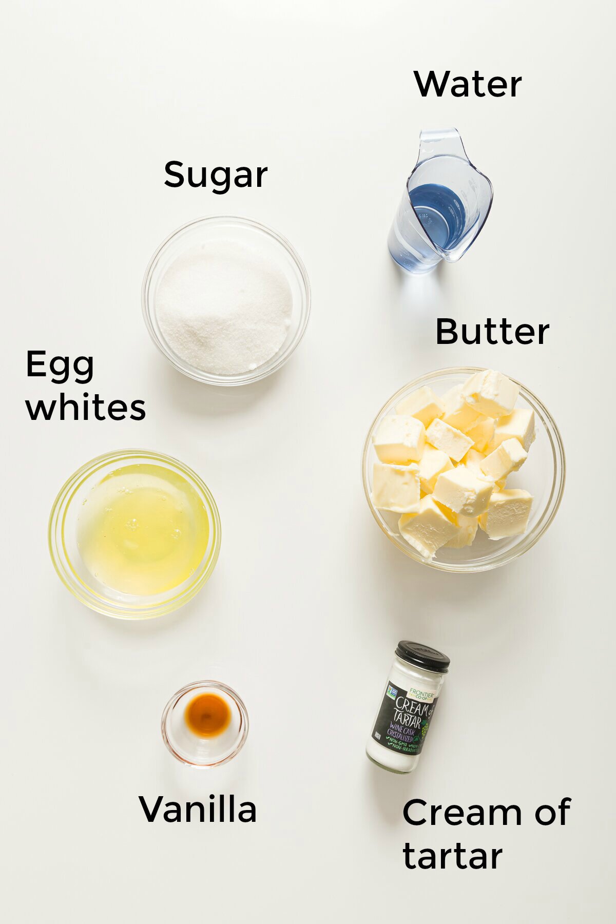 top-down view of ingredients needed to make Italian meringue buttercream frosting: sugar, water, egg whites, butter, vanilla extract, and cream of tartar