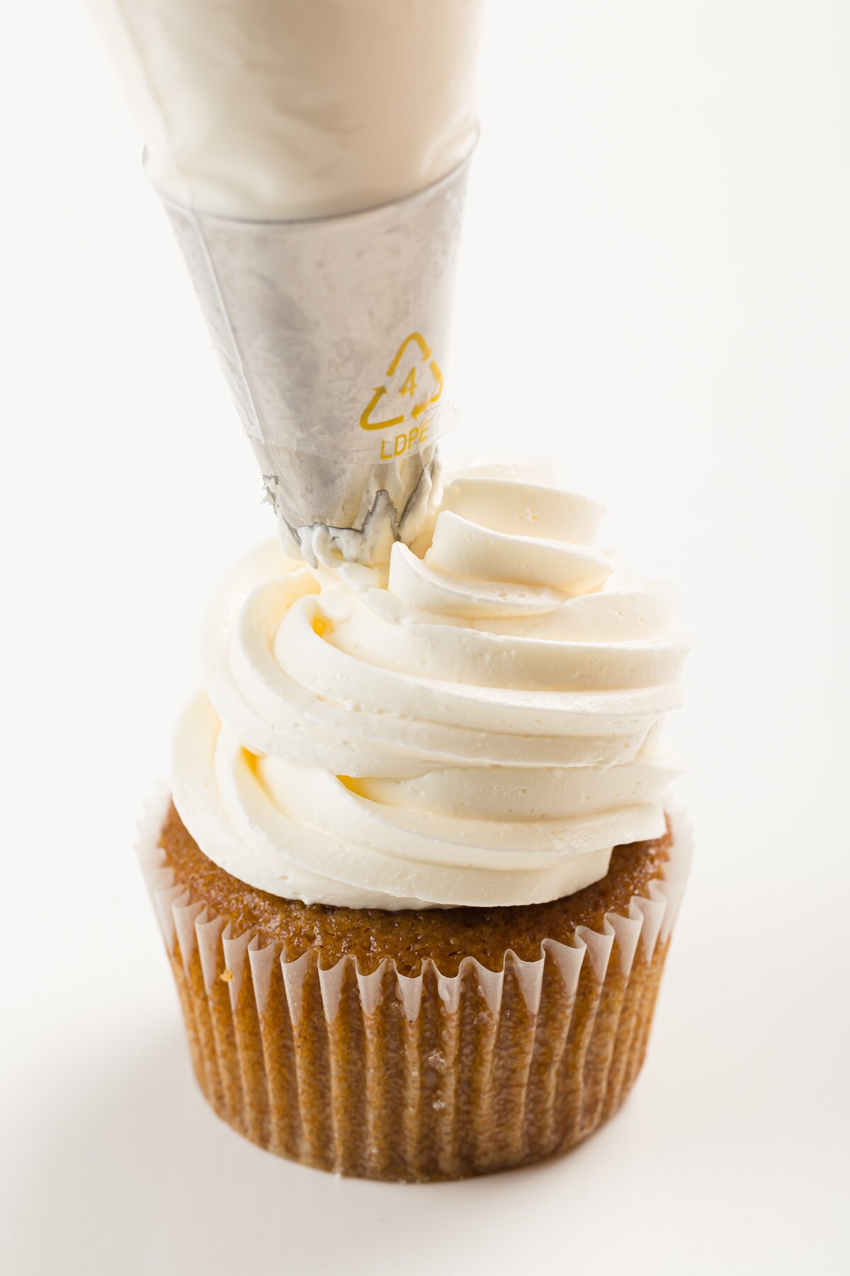 Italian meringue buttercream frosting being piped onto a cupcake