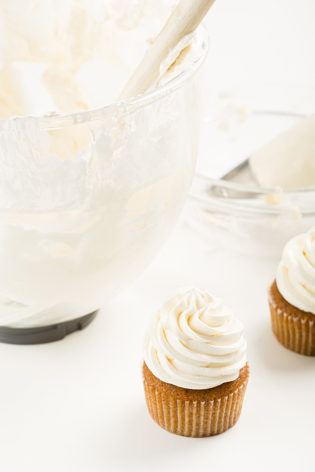 a cupcake frosted with Italian meringue buttercream frosting with a bowl of frosting behind it
