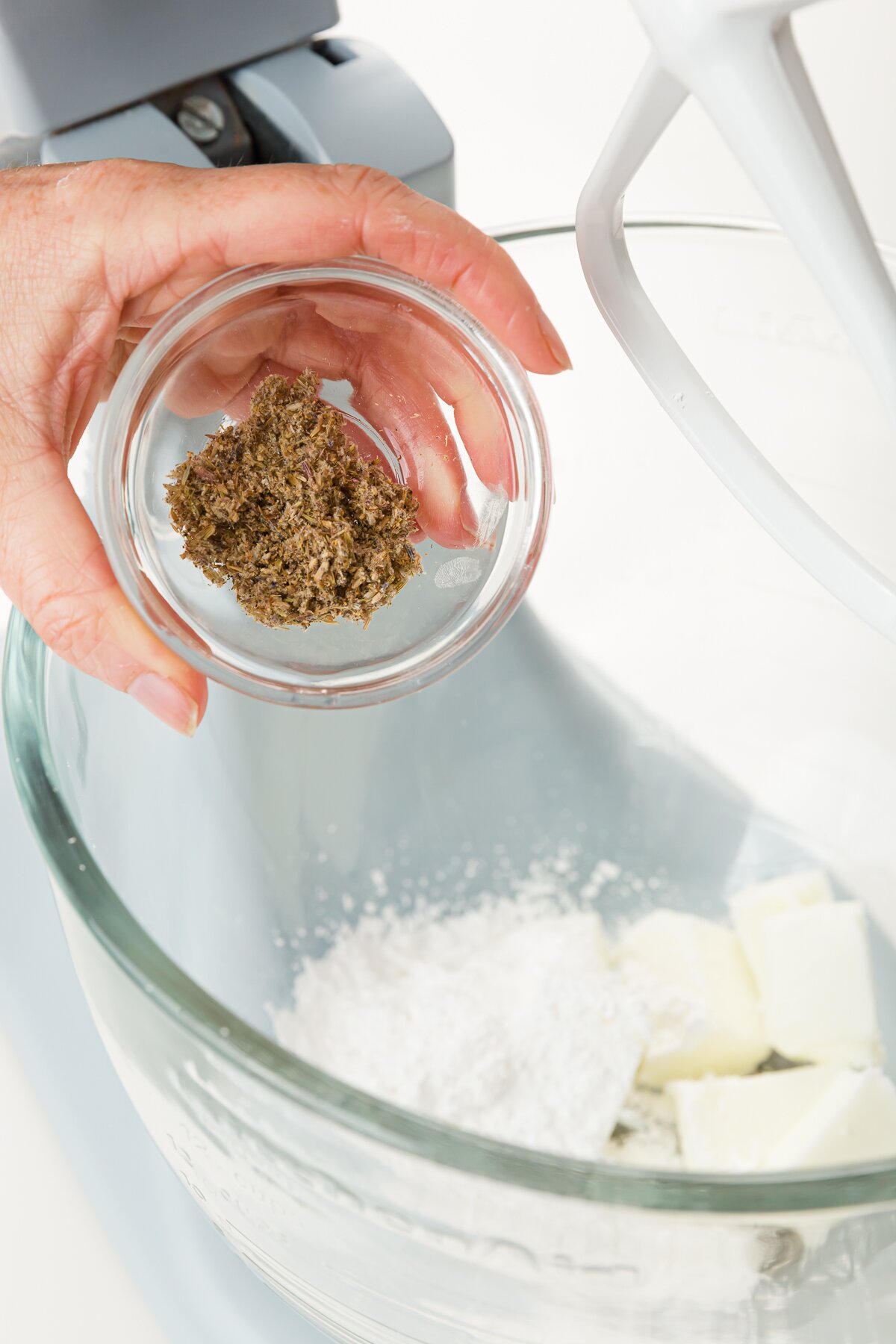 Holding a bowl of lavender over a stand mixer bowl filled with butter and powdered sugar