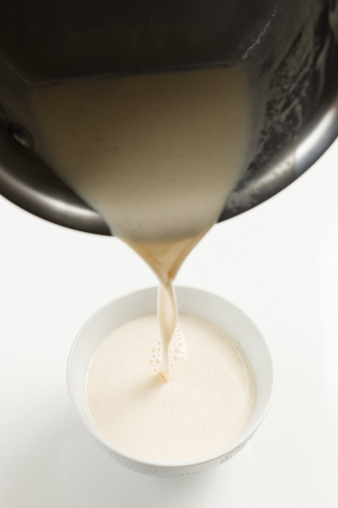 warm panna cotta being poured from a pot into a ramekin