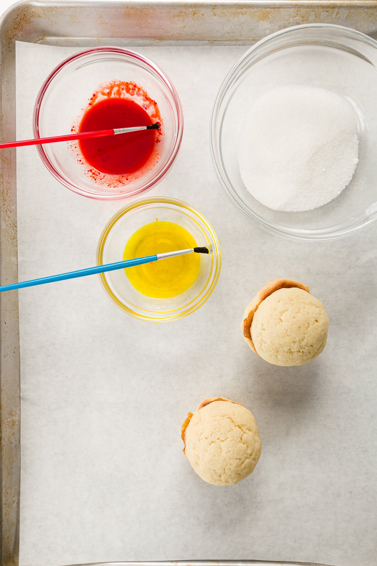 One bowl of red liquid, one bowl of yellow liquid, two cookies, and bowl of sugar