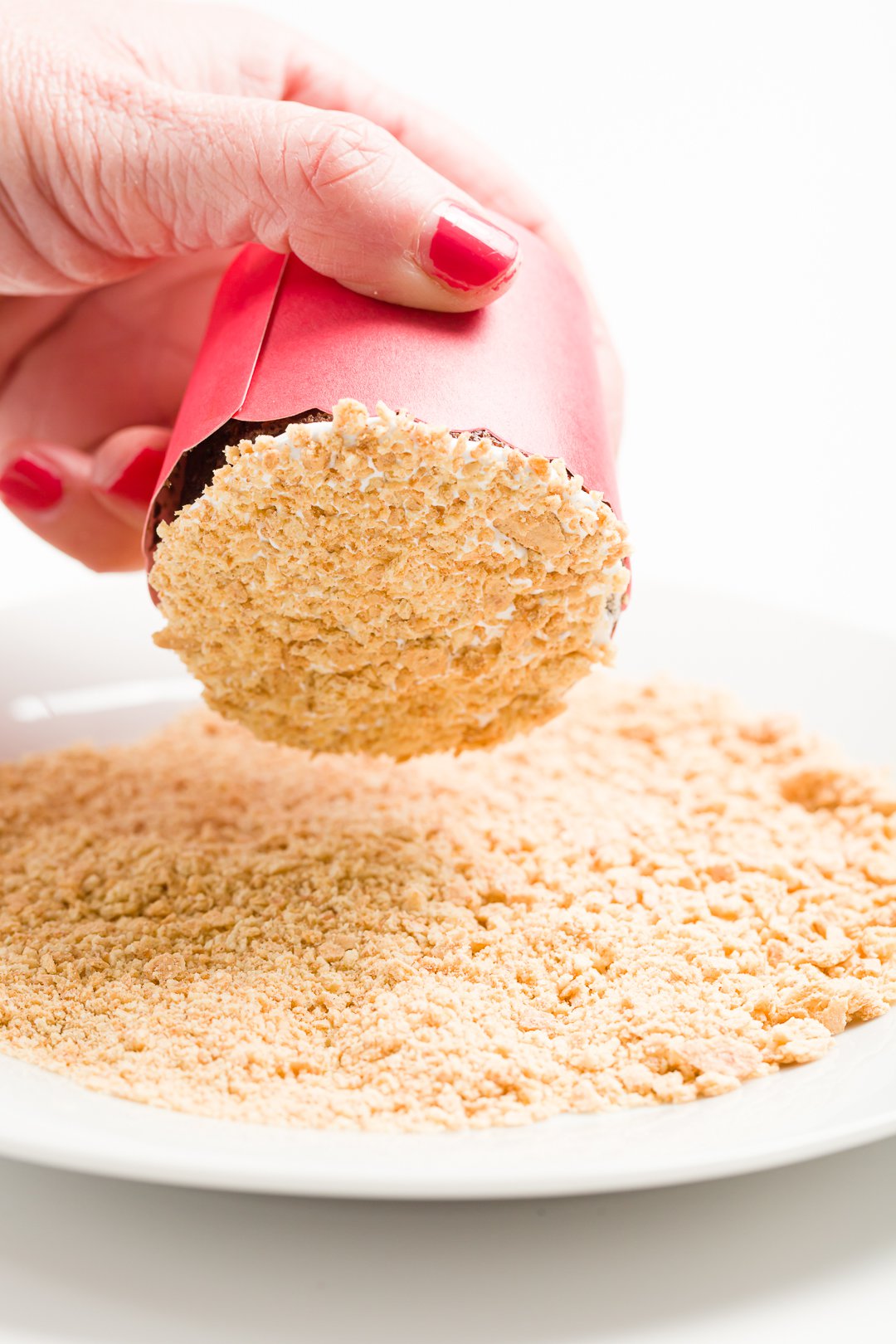 head-on view of inverting a s'mores cupcake with a thin layer of marshmallow frosting onto a plate full of crushed graham crackers