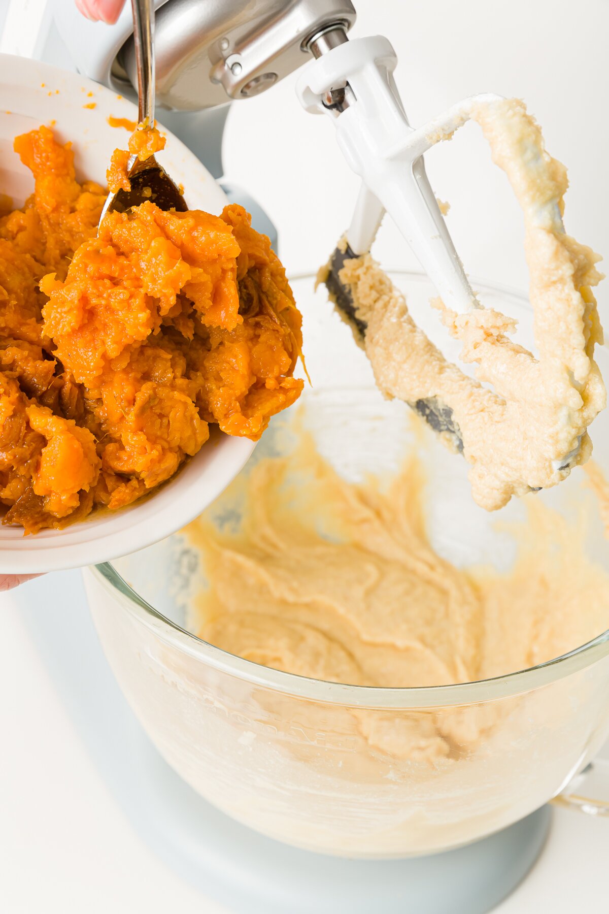 Adding mashed sweet potatoes to a KitchenAid mixer with a blade raised