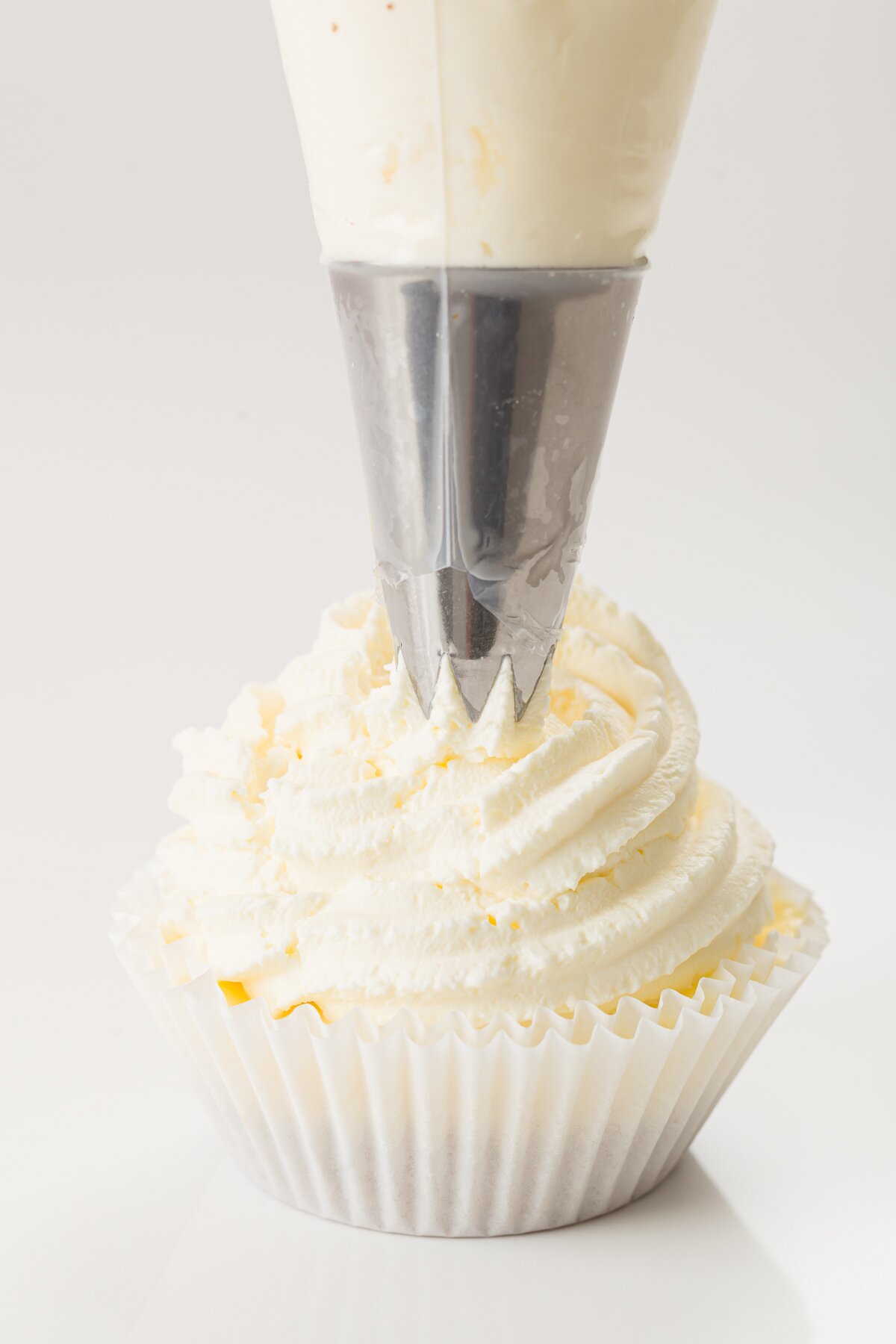 tight shot of Stef piping whipped cream on top of a tiramisu cupcake