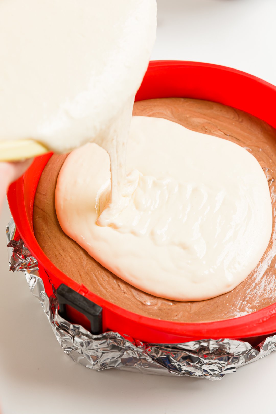 Pouring vanilla cheesecake over chocolate cheesecake