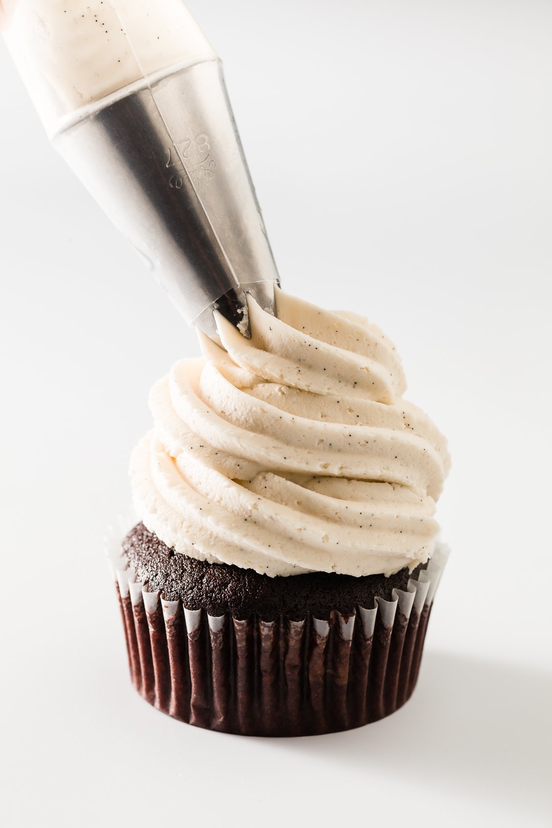 Vanilla buttercream frosting being piped onto a chocolate cupcake