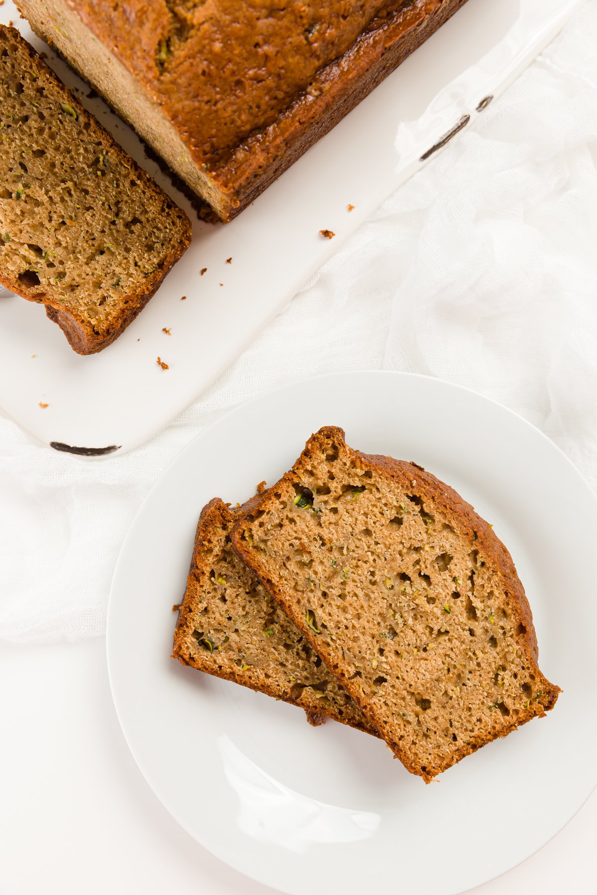 two slices of zucchini bread on a while plate with the loaf in the background